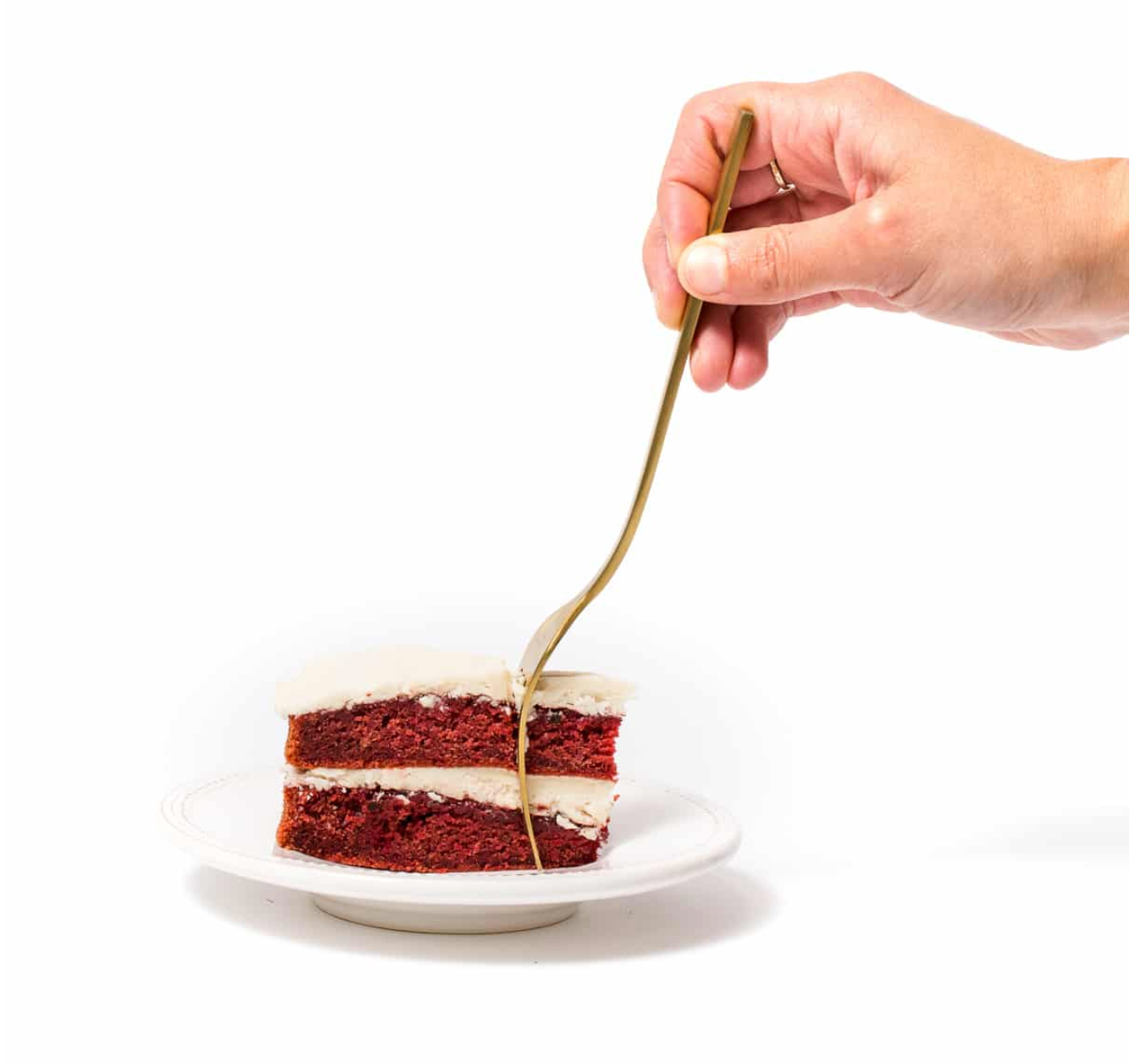 A hand holding a fork inserted in a slice of Miss Jones Baking Beet Red Velvet Cake